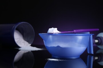 Blonde hair care cosmetic product. Powder in bowl, jar and spatula on black mirror surface against dark purple background, closeup