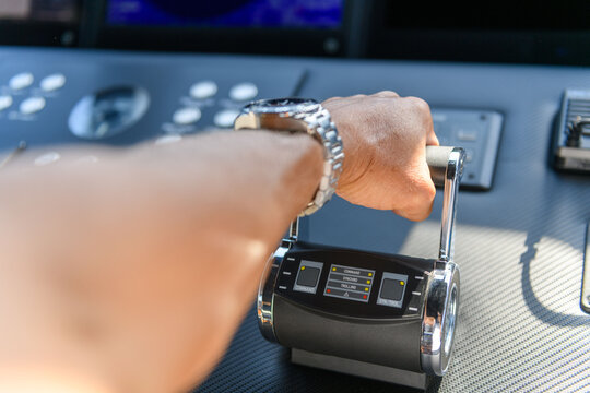 A close-up view of a yacht or ship bridge with a person’s hand operating the throttle controls. The navigation radar screen and electronic control panels are visible in the background