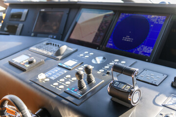 A close-up view of a yacht or ship bridge with the throttle controls. The navigation radar screen and electronic control panels are visible in the background