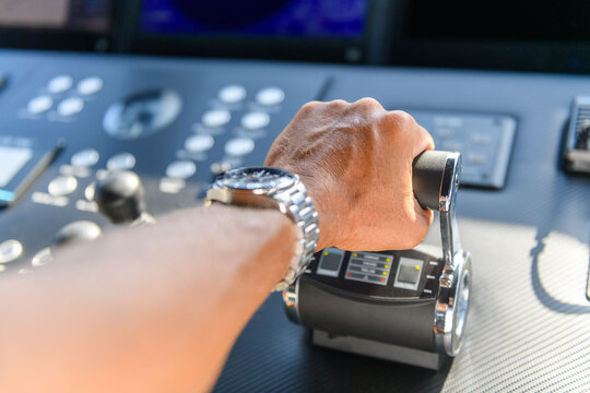 A close-up view of a yacht or ship bridge with a person’s hand operating the throttle controls. The navigation radar screen and electronic control panels are visible in the background