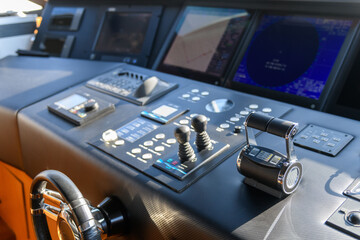 A close-up view of a yacht or ship bridge with the throttle controls. The navigation radar screen and electronic control panels are visible in the background