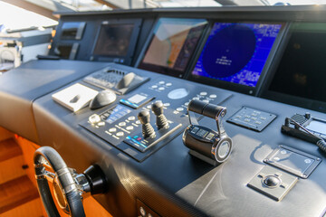 A close-up view of a yacht or ship bridge with the throttle controls. The navigation radar screen and electronic control panels are visible in the background