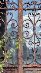 Close-up of an old, rusty wrought iron gate with intricate scrollwork and reflected sky