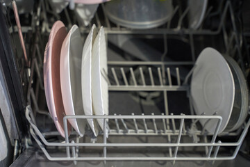 Clean dishes in open dishwasher with neatly arranged plates and bowls for efficient kitchen...