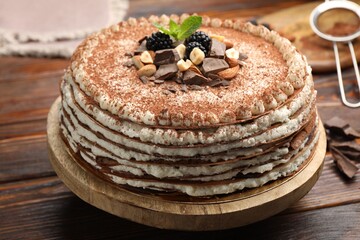 Delicious crepe cake with chocolate, nuts, blackberries and cocoa powder on wooden table, closeup