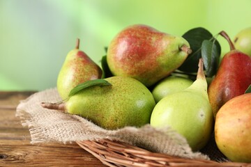 Fresh ripe pears with green leaves in wicker basket on wooden table, closeup
