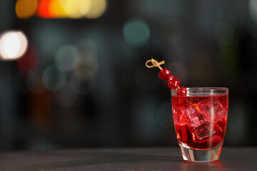 Glass of alcoholic cocktail with cherries on table against blurred background. Space for text