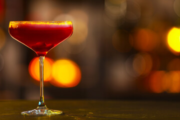 Glass of alcoholic cocktail on table against blurred background. Space for text