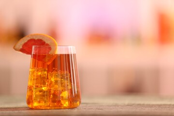 Glass of alcoholic cocktail with grapefruit slice on wooden table against blurred background. Space for text