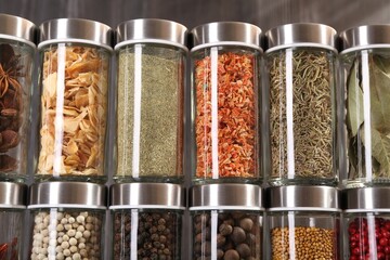 Different spices in glass jars against grey background, closeup
