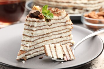 Piece of tasty crepe cake with cocoa powder, chocolate and nuts served on light table, closeup