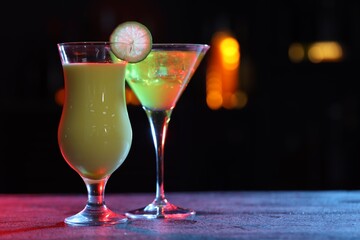 Glasses of alcoholic cocktails with garnish on table against blurred background, space for text. Bokeh effect