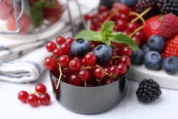 Ripe red currants, blueberries and mint leaves in scoop on white tiled table, closeup