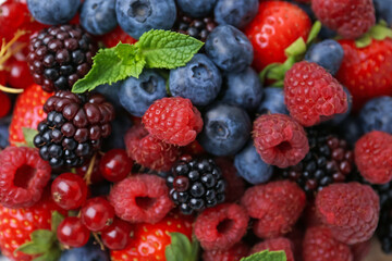 Different ripe berries and mint leaves as background, above view