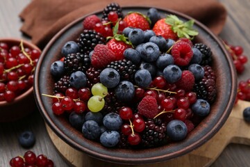 Different ripe berries in bowl on wooden table, closeup