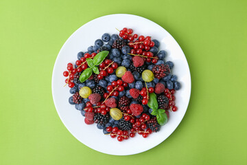 Different ripe juicy berries on plate against green background, top view