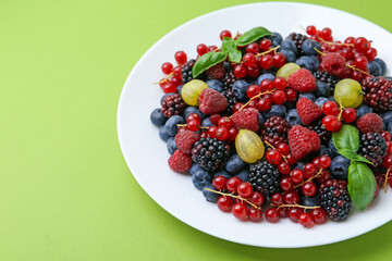Different ripe juicy berries on plate against green background, closeup. Space for text