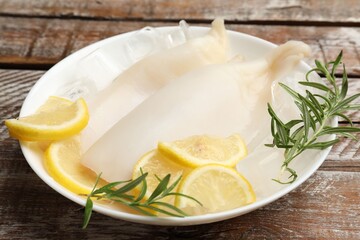 Pieces of raw squids with ice cubes, rosemary and lemon on color wooden table, closeup