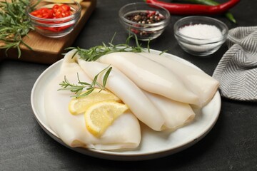 Uncooked squids with lemon slices, rosemary and spices on black table, closeup