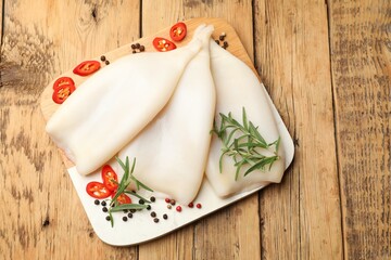 Uncooked squids with spices on wooden table, top view