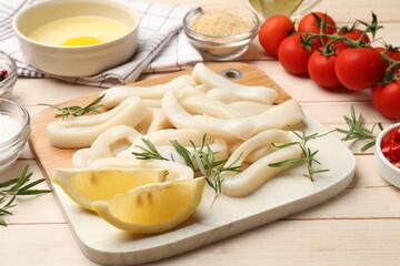 Uncooked squid rings, spices, yolk, tomatoes and bread crumbs on wooden table, closeup