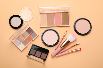 Fototapeta premium Colorful eyeshadow palettes, powders, makeup brushes and applicator on beige background, flat lay