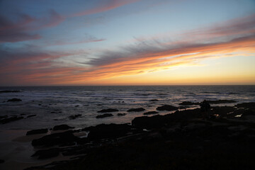 Obraz premium Rocky coastline of Portugal at sunset. People on the rocks, pastel sky, waves, foam, peaceful scene, natural depth, dramatic atmosphere.