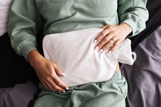 Woman using hot water bottle for period cramps. Natural relief for abdominal pain. Cozy home remedy against menstrual discomfort. Health care with traditional solution. Resting on bed in comfort.