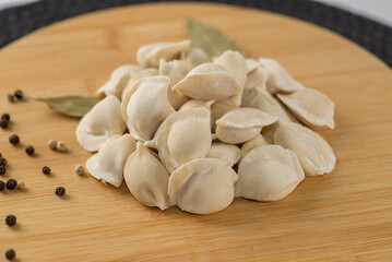 Frozen dumplings semi-finished product piled up decorated with spices on a board