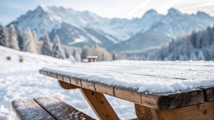 Snow-covered picnic table in alpine mountains. Wooden picnic table dusted with fresh snow, set in a scenic winter mountain landscape with pine trees and distant peaks