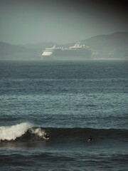 Two surfers catching waves on the beach with the ocean, the cruise ship, and the coast in the background.
