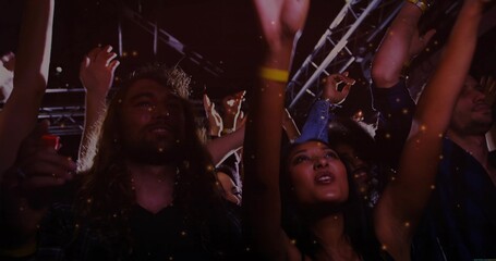 Cheering fans moving under metal trusses at concert hall, with spotlights wristbands and confetti