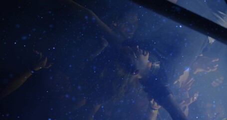 Lifting crowd surfer wearing spiked necklace at concert under blue lights, with confetti drifting