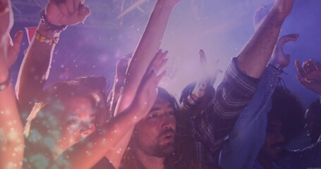 Dancing group of five concert fans celebrating under purple, pink lights amid haze and metal truss