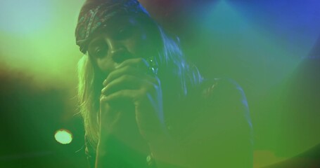 Singing female singer wearing patterned bandana on stage, with handheld microphone and haze