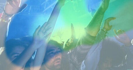 Raising arms five friends dancing at live music venue, with colored beams cutting haze