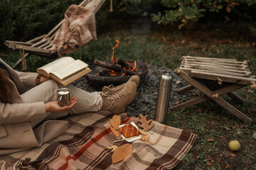 Cozy autumn scene with a person reading by a campfire