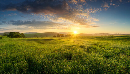 Obraz premium Vibrant Green Meadow At Sunrise Or Sunset The Colorful Summer Sky And Golden Sunlight Casting A Warm Glow Over The Wide Tranquil Landscape Creating A Peaceful And Beautiful Morning Panorama