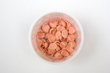 A bowl of pinky colored crispy corn flake cereal isolated on white background.