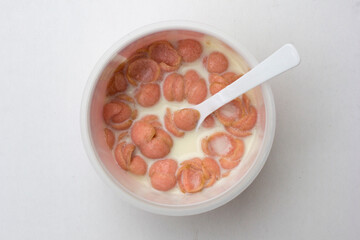 A bowl of pinky colored crispy corn flake cereal with milk isolated on white background.