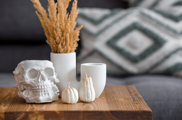 Halloween celebration. A white skull, candles and pumpkins on the table. Decor for the Day of the...