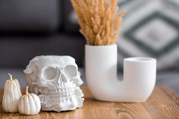Halloween celebration. A white skull, candles and pumpkins on the table. Decor for the Day of the Dead or Halloween in the living room interior.