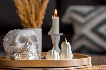 Halloween celebration. A white skull, candles and pumpkins on the table. Decor for the Day of the Dead or Halloween in the living room interior.