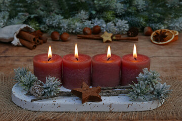 Fourth Advent: Decoration with rust-colored candles, cinnamon sticks, orange slices, and nuts in front of fir branches with space for text.