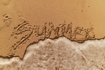 Writing summer in the sand as waves gently lap at the shore during a sunny beach day