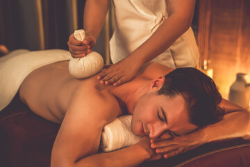 Hot herbal ball spa massage body treatment, masseur gently compresses herb bag on man body....