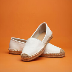 Pair of white espadrille shoes on orange background. Stylish footwear. Leather loafers with a natural woven jute sole. Summer fashion concept for casual style.