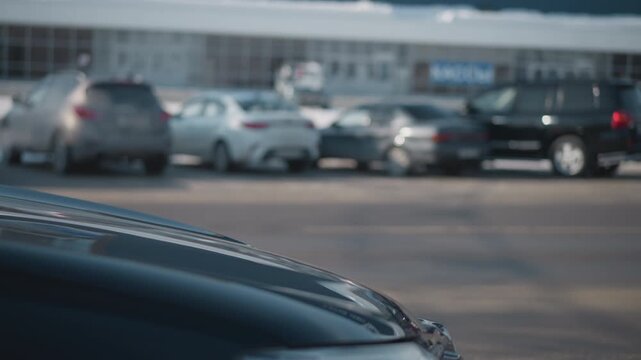 cars parked on both sides of street with vehicles driving along busy urban road, blurred motion, clear daylight, asphalt pavement, building facade in background, winter season with snow accumulation
