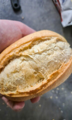 Close-up of a hand holding a freshly baked bread roll, showcasing the golden crust and soft inner texture, ideal for culinary themes, food photography, and bakery promotions.