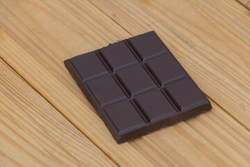 Dark chocolate bar with square pieces placed on wooden background, sweet dessert concept with rich cocoa flavor